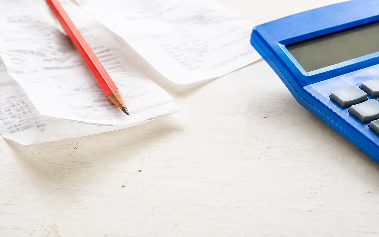A cobalt blue calculator and coral pencil beside paper receipts on a bright tabletop.