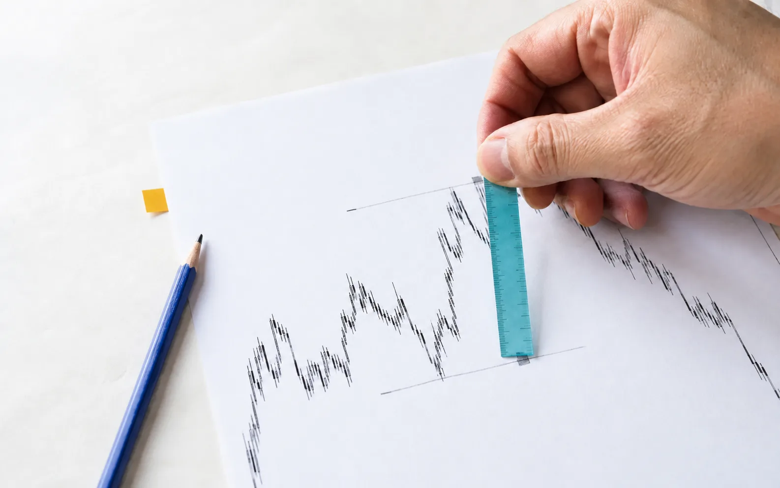 A hand measures marked risk levels on a paper chart with a teal ruler beside a blue pencil.